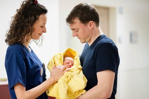 Vater mit Neugeborenem und einer Mitarbeiterin