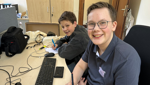 Christian und Moritz sitzen am Schreibtisch und schreiben den Text auf Tablet und Block