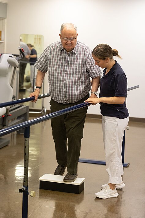 Physiotherapeutin mit Patient beim Gehtraining am Stufenbarren