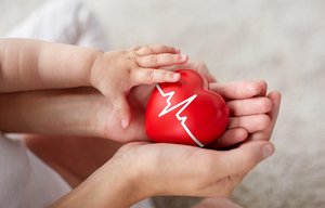 Erwachsene Hand und Babyhand halten ein kleines Herzsymbol